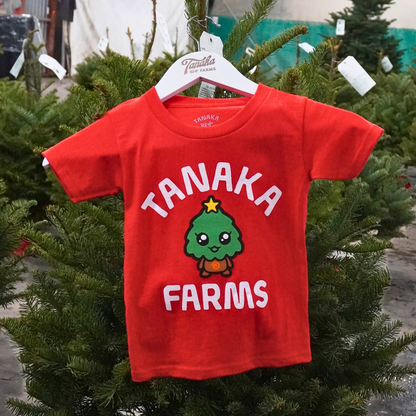 Red t-shirt with 'Tanaka Farms' text and logo on a hanger amidst Christmas trees.